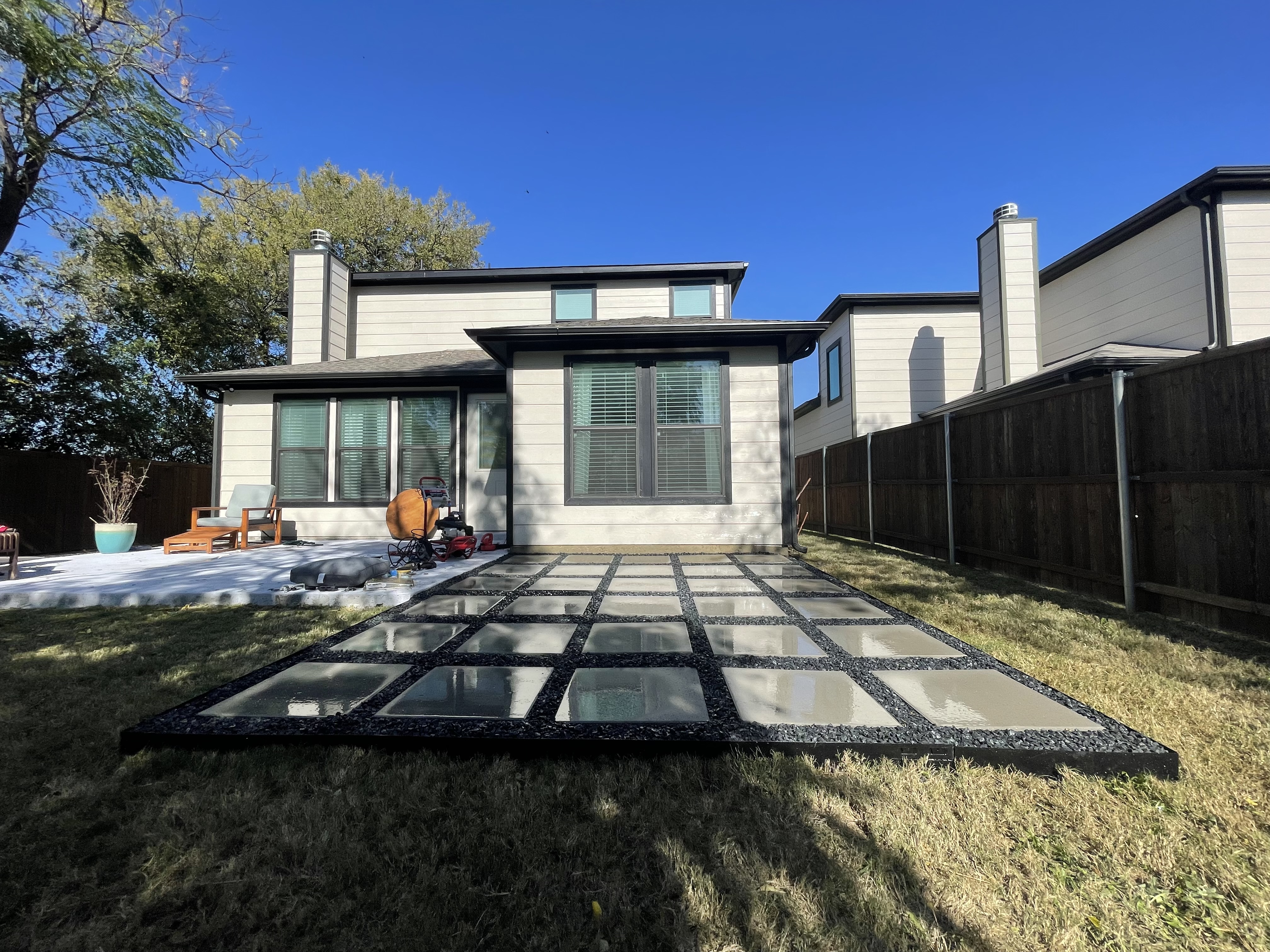 Large-format concrete paver patio with black gravel joints installed across a DFW backyard behind a two-story home, by Loera's Landscaping