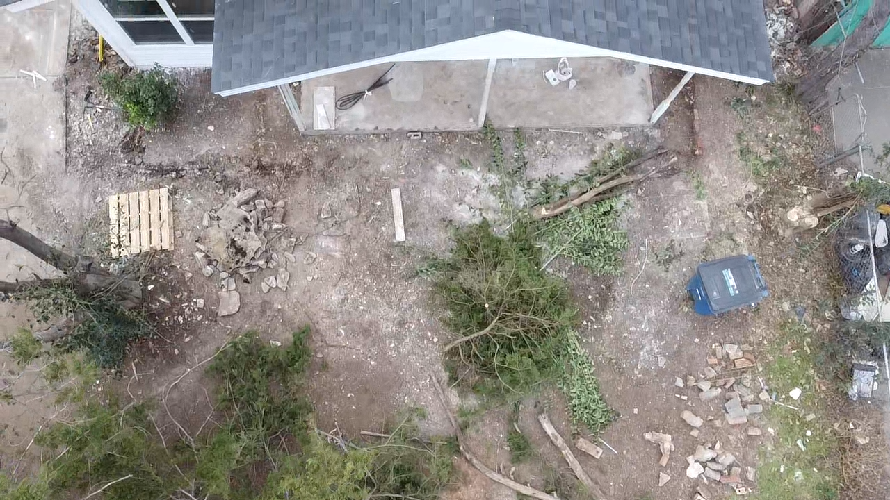 Overhead drone view of the front lot before work, showing bare rutted dirt, scattered brush, and stacked debris