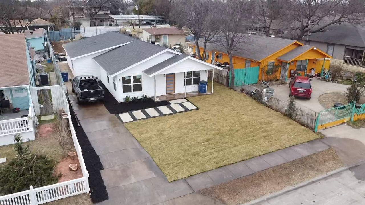 The same front yard after clearing, with fresh sod covering the lot, a paver walkway to the porch, and a mulched bed along the driveway