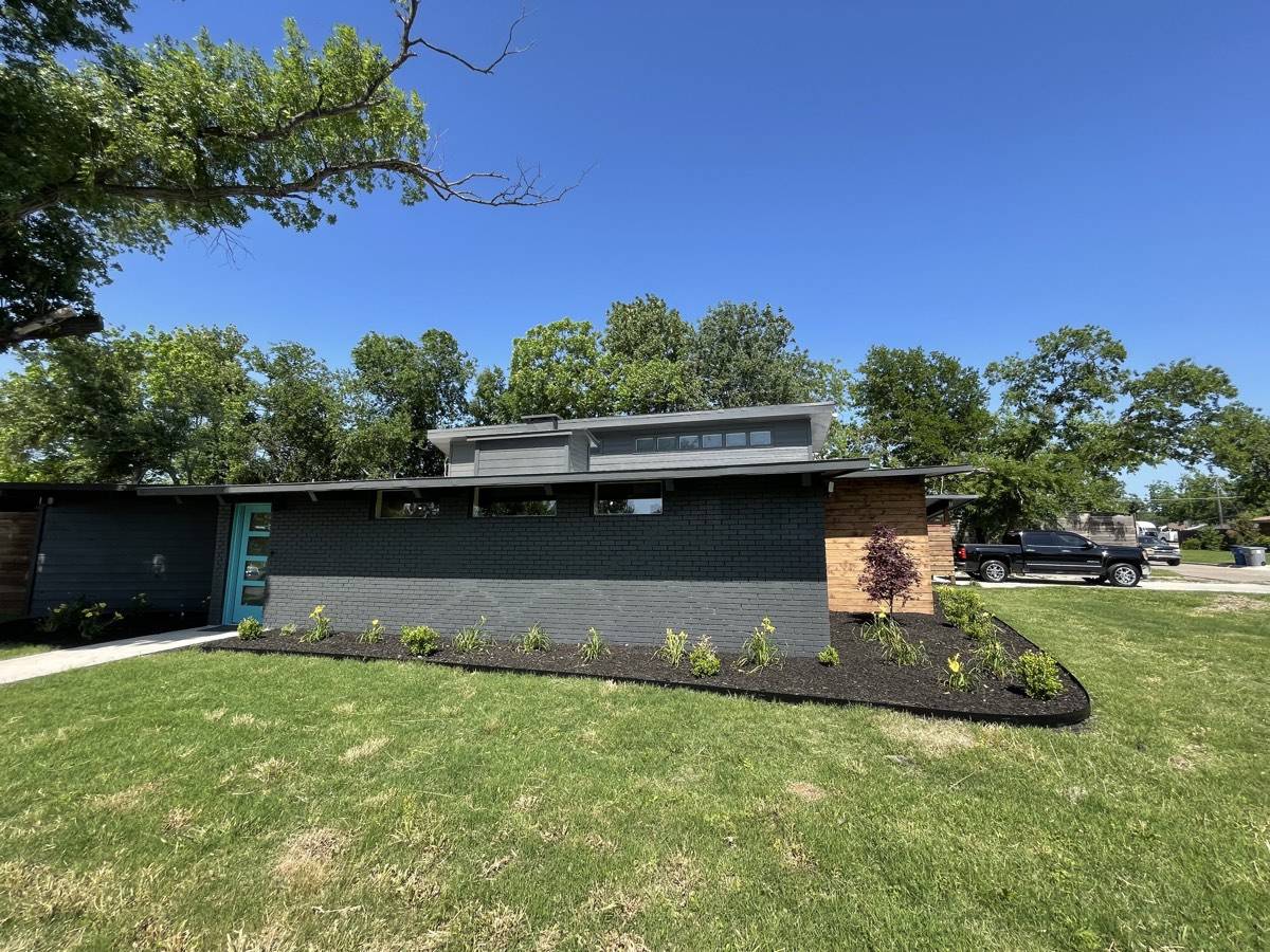 New front-yard planting bed with fresh mulch and young shrubs along a modern home